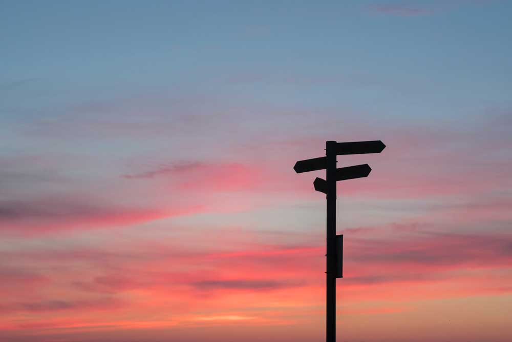 A silhouette of directionals on a post is backlit by a sunset with orange, red, pink, and blue colors.