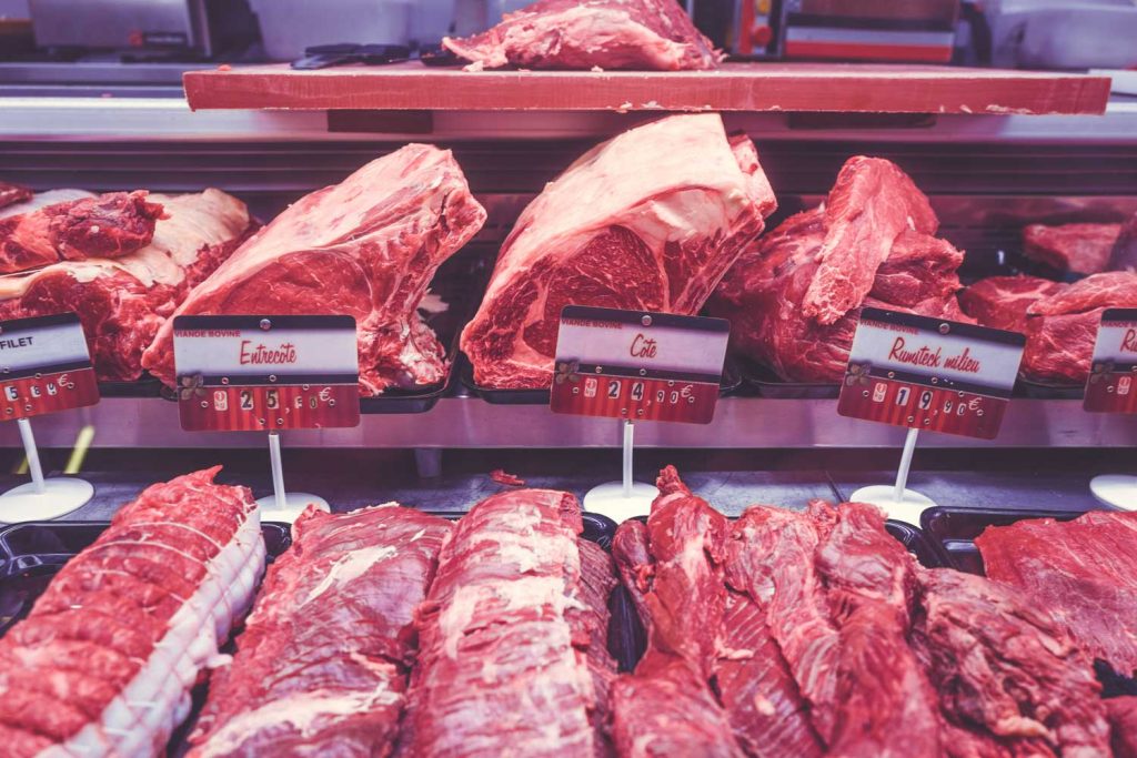 [An array of butchered meat sits on trays inside a display case. Price tags are on a stick and in Spanish.]