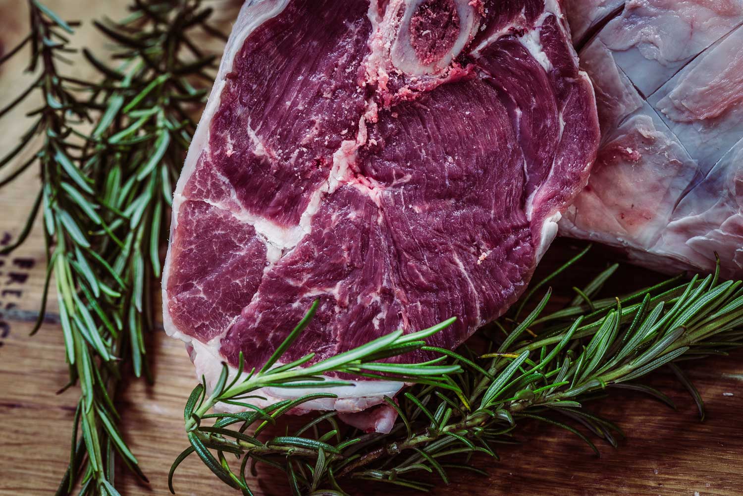 [A slab of butchered meat lays on a cutting board, surrounded by fat and fresh rosemary.]