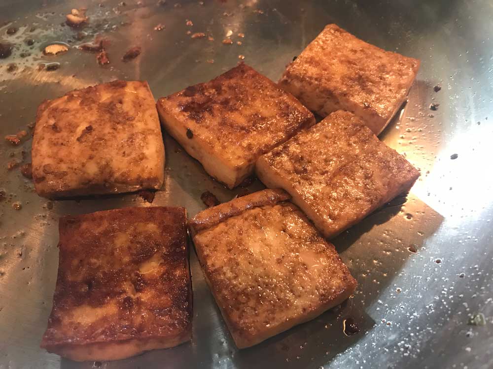 Golden brown square pieces of tofu is on top of a stainless steel pan.